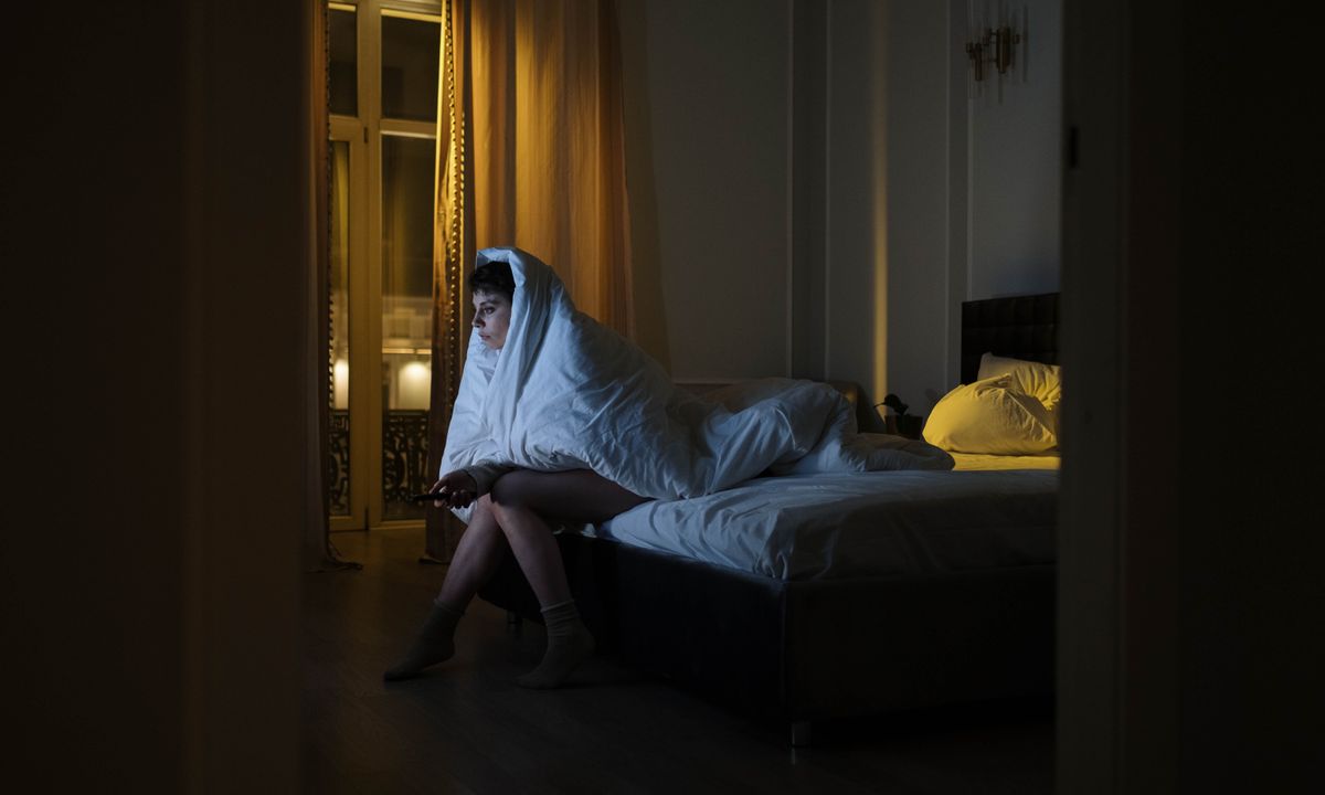 A woman awake at night, wrapped in a duvet on the edge of her bed
