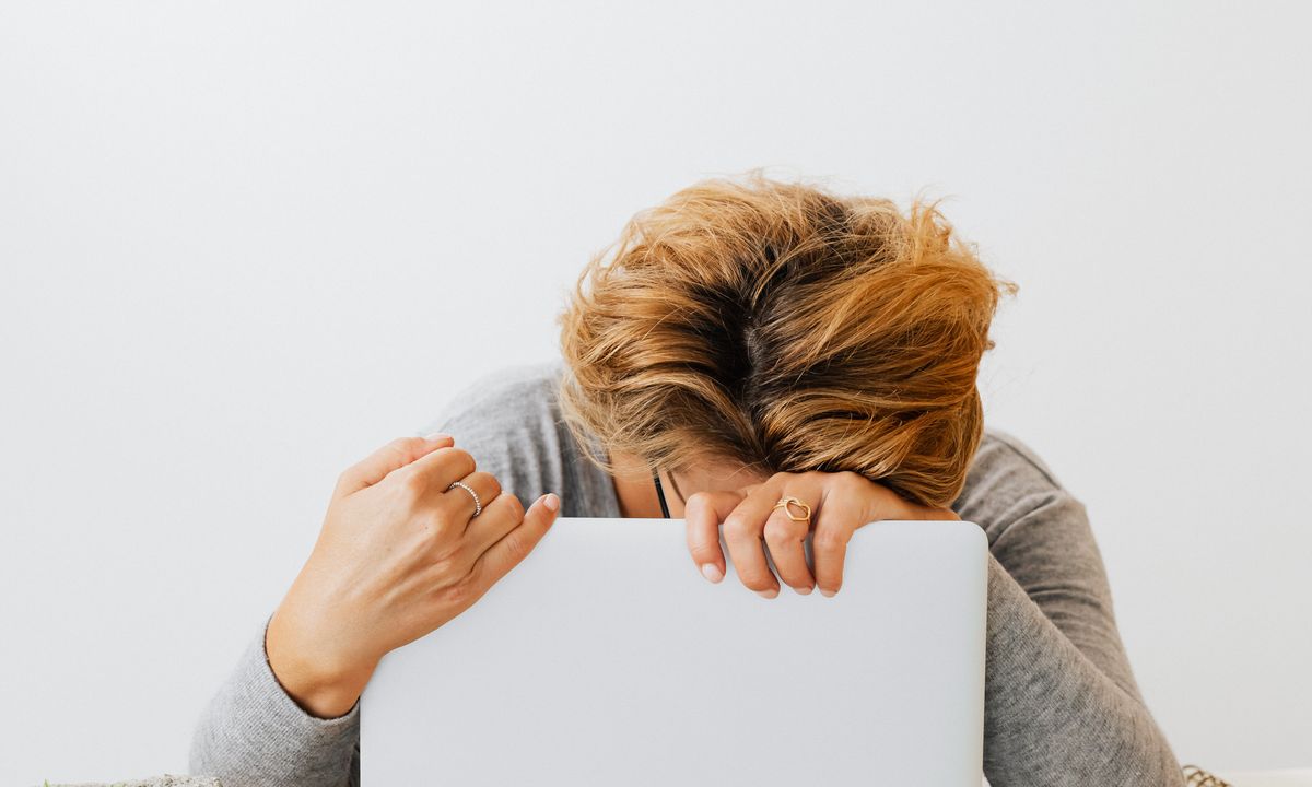 An exhausted woman resting her head on a laptop